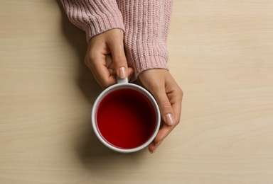 Photo of Woman holding cup of tea at wooden table, top view