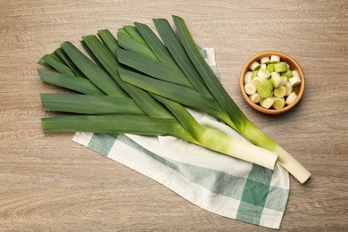Whole and cut fresh leeks on wooden table, flat lay