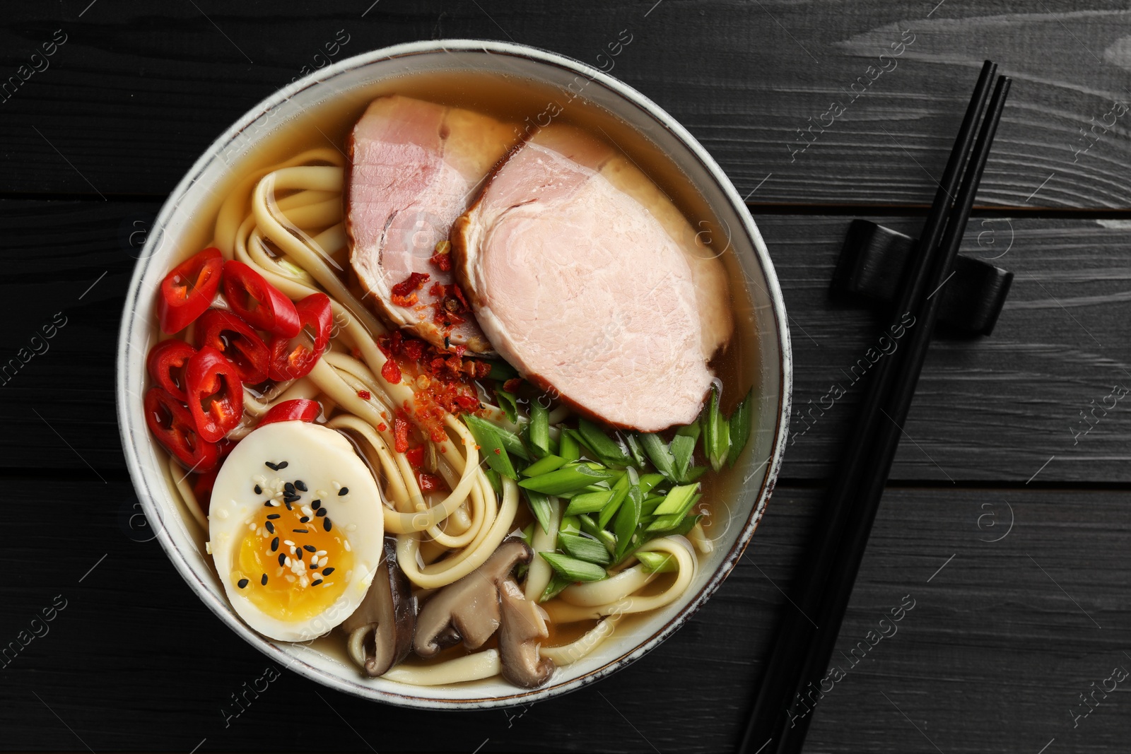 Photo of Delicious ramen in bowl and chopsticks on black wooden table, flat lay. Noodle soup