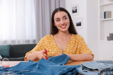 Happy woman cutting hem of jeans at table indoors