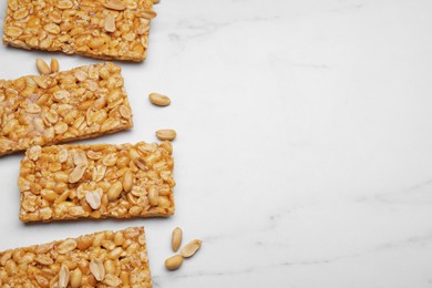 Delicious peanut bars (kozinaki) and nuts on white marble table, flat lay. Space for text