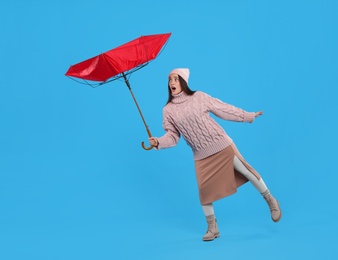 Emotional woman with umbrella caught in gust of wind on light blue background