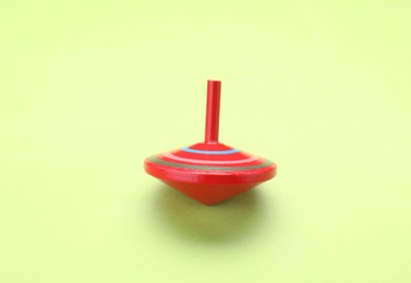Photo of One bright spinning top on light green background. Toy whirligig