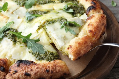 Photo of Taking slice of delicious pizza with pesto, cheese and arugula on table, closeup