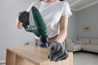 Photo of Woman with electric screwdriver assembling furniture at home, closeup