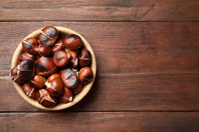 Photo of Delicious roasted edible chestnuts on brown wooden table, top view. Space for text
