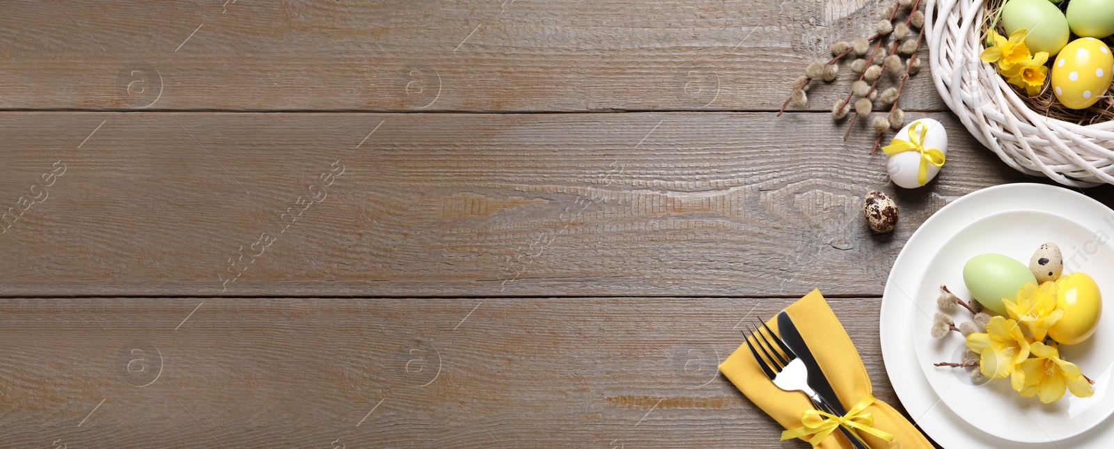 Image of Festive Easter table setting with painted eggs and flowers on wooden background, flat lay. Space for text