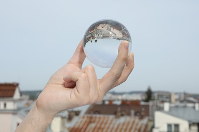 Photo of View of beautiful city street, overturned reflection. Man holding crystal ball outdoors, closeup