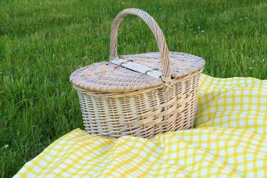 Photo of Picnic basket with checkered tablecloth on green grass outdoors