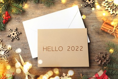 Image of Card with text Hello 2022, envelope and Christmas decor on wooden table, flat lay