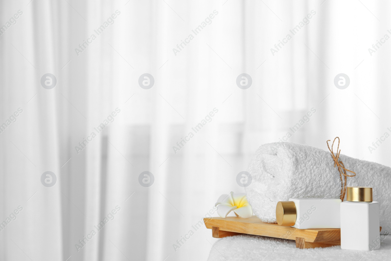 Photo of Cosmetic bottles and fresh towel on table indoors, space for text. Spa treatment