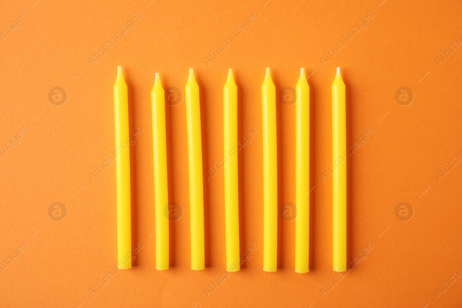 Photo of Yellow birthday candles on orange background, top view