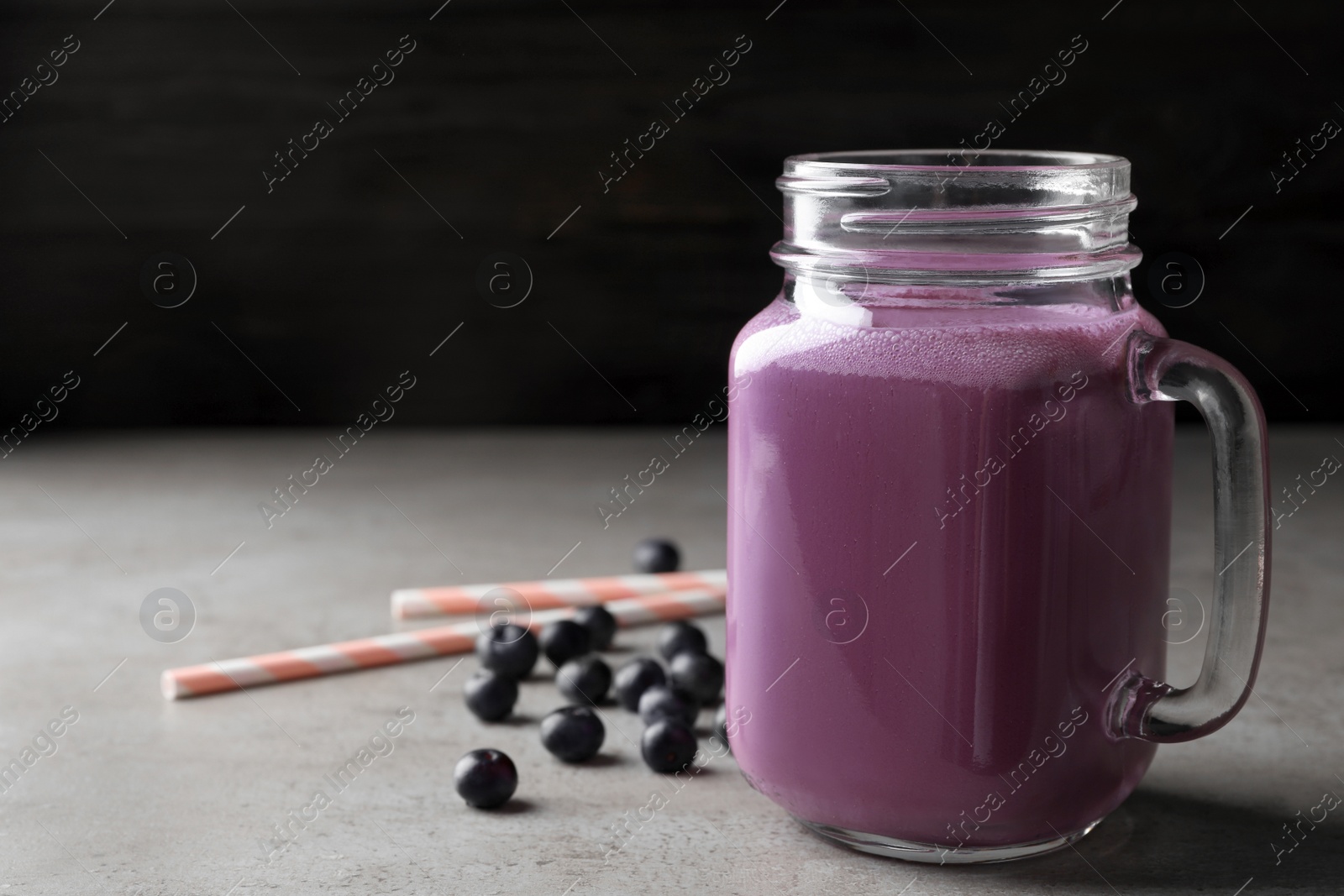 Photo of Tasty acai drink in mason jar  and berries on grey table, space for text