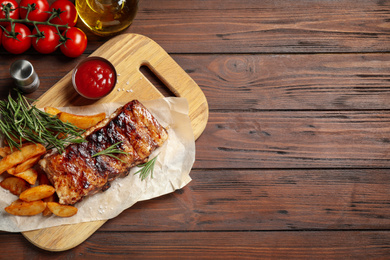 Delicious grilled ribs and garnish on wooden table, flat lay. Space for text