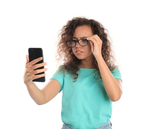 Young African-American woman with vision problems using smartphone on white background