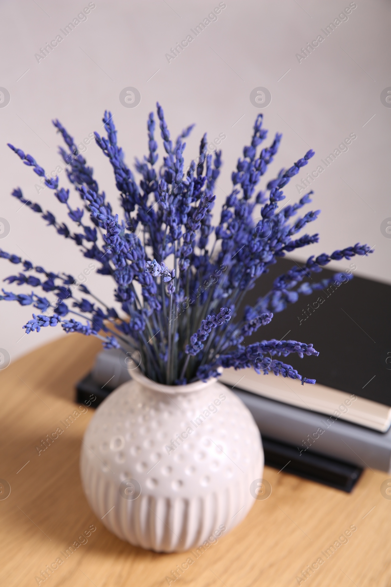 Photo of Bouquet of beautiful preserved lavender flowers and notebooks on wooden table near beige wall, closeup