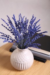 Bouquet of beautiful preserved lavender flowers and notebooks on wooden table near beige wall, closeup