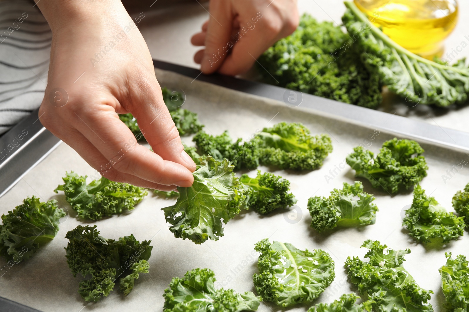 Photo of Woman preparing kale chips at table, closeup