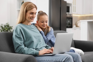 Happy woman and her daughter with laptop on sofa at home