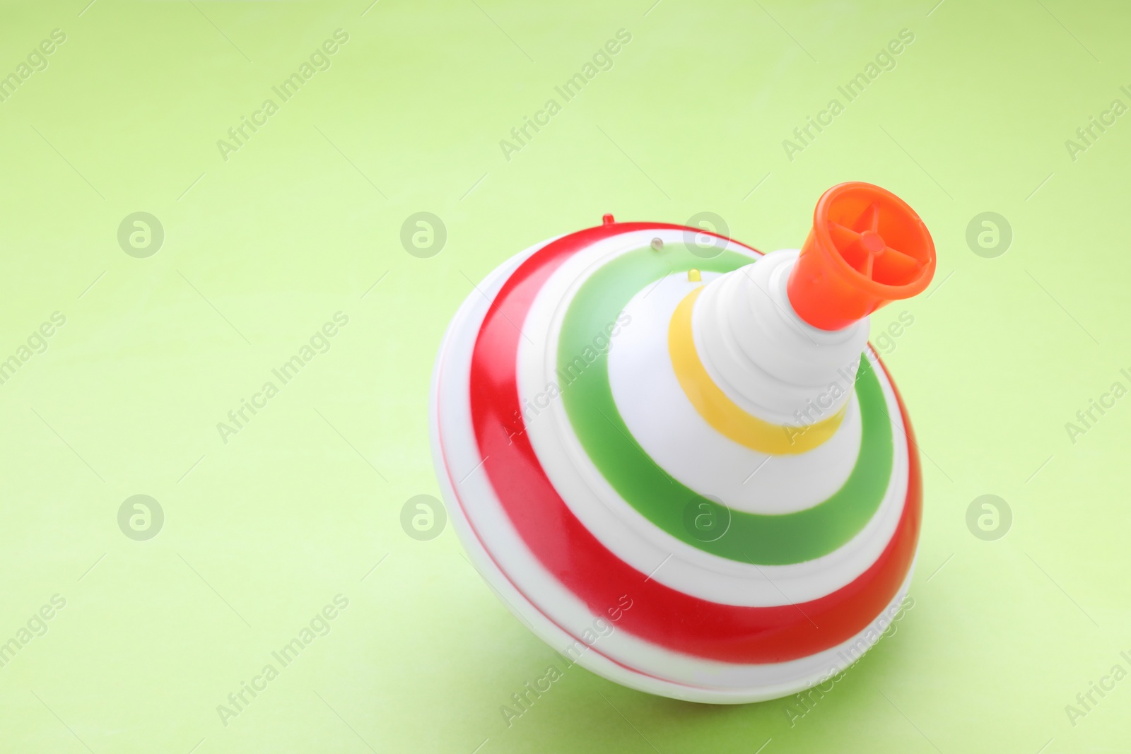 Photo of One bright spinning top on light green background, closeup with space for text. Toy whirligig