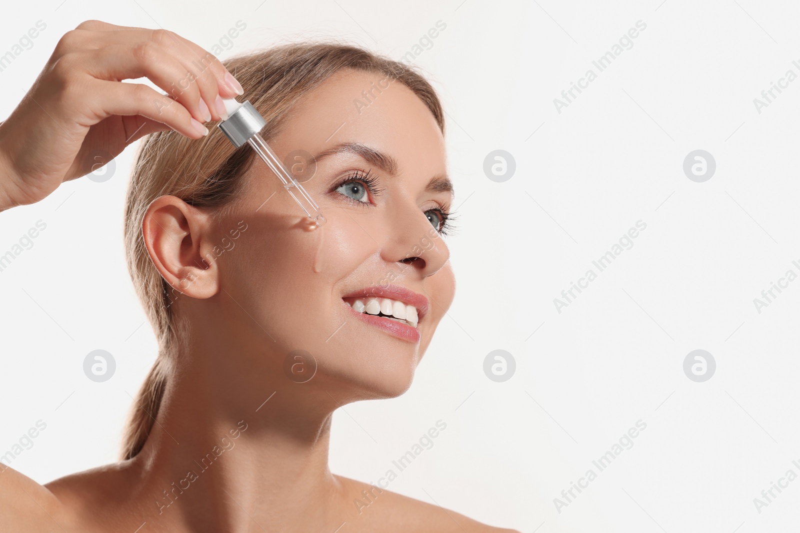 Photo of Beautiful woman applying cosmetic serum onto her face on white background, space for text