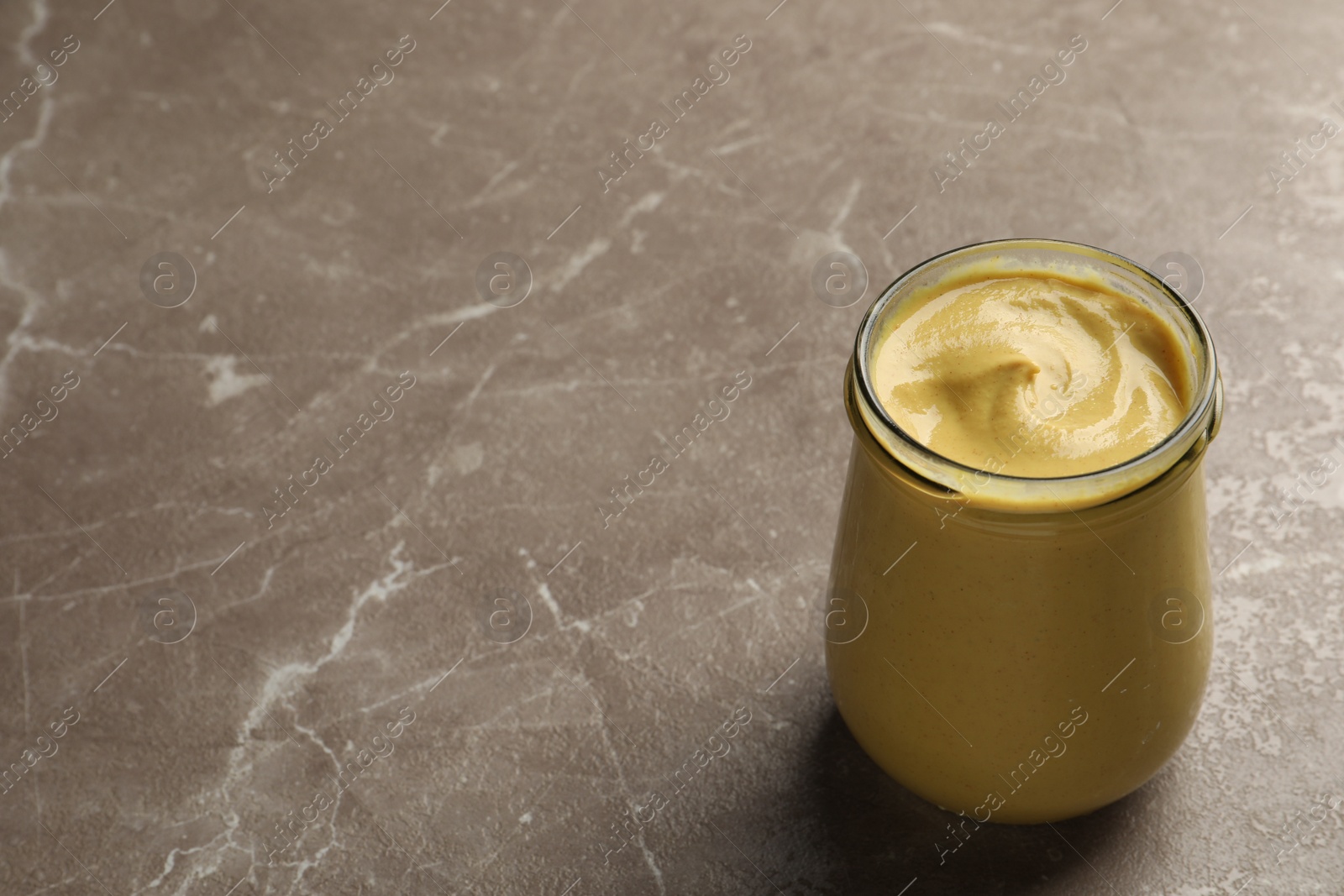 Photo of Spicy mustard in glass jar on brown marble table. Space for text