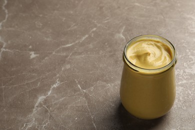 Spicy mustard in glass jar on brown marble table. Space for text