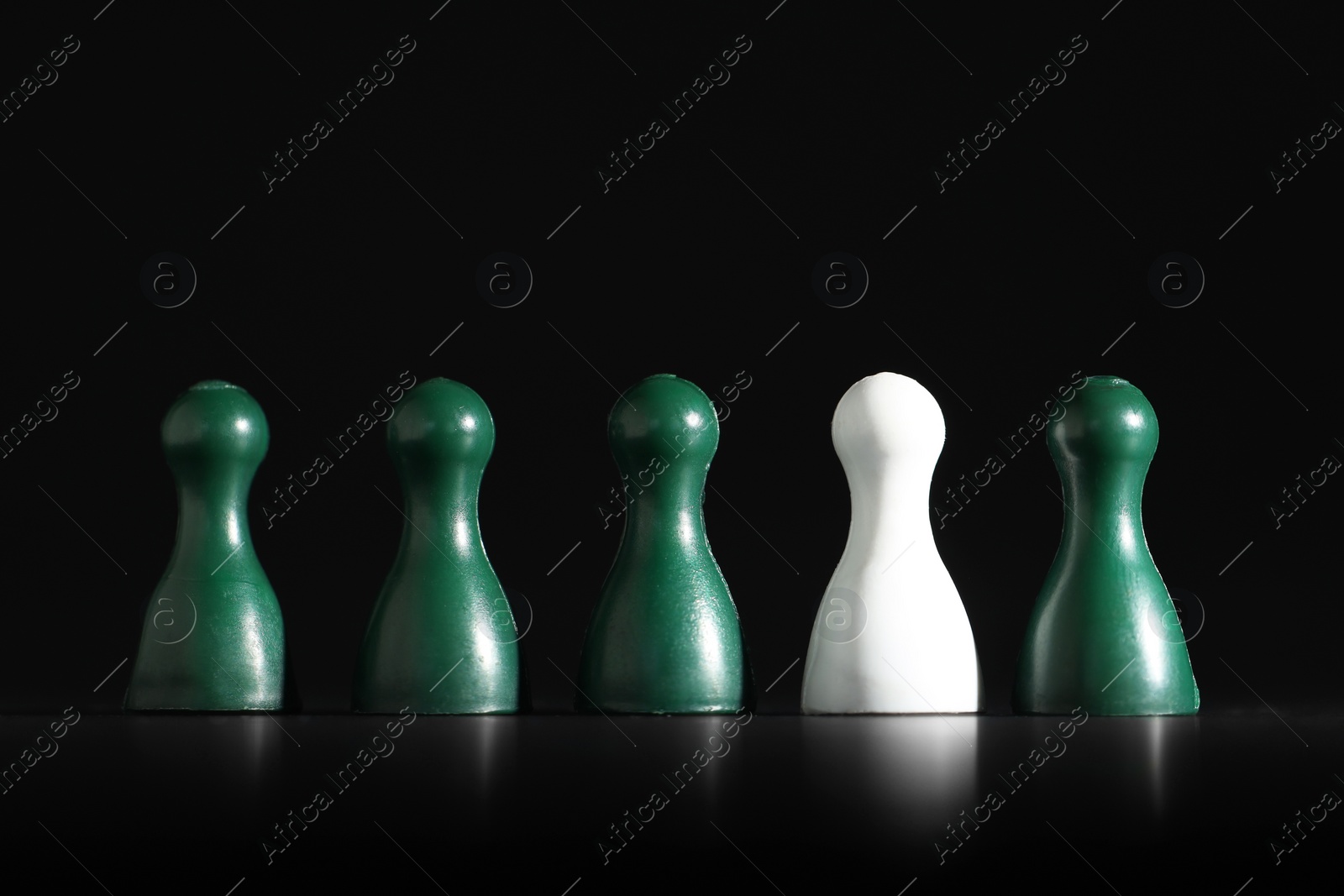 Photo of Choice concept. White pawn among green ones on black table, closeup