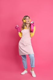 Photo of Beautiful young woman with headphones, rag and bottledetergent singing on pink background