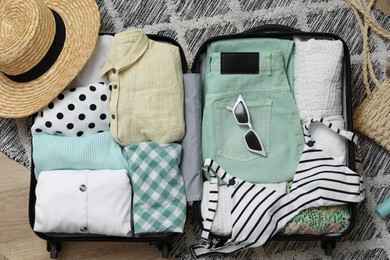 Open suitcase with summer clothes and accessories on floor, flat lay