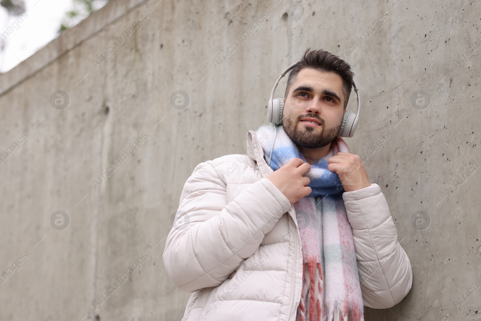 Photo of Handsome man in warm scarf and headphones near wall outdoors. Space for text