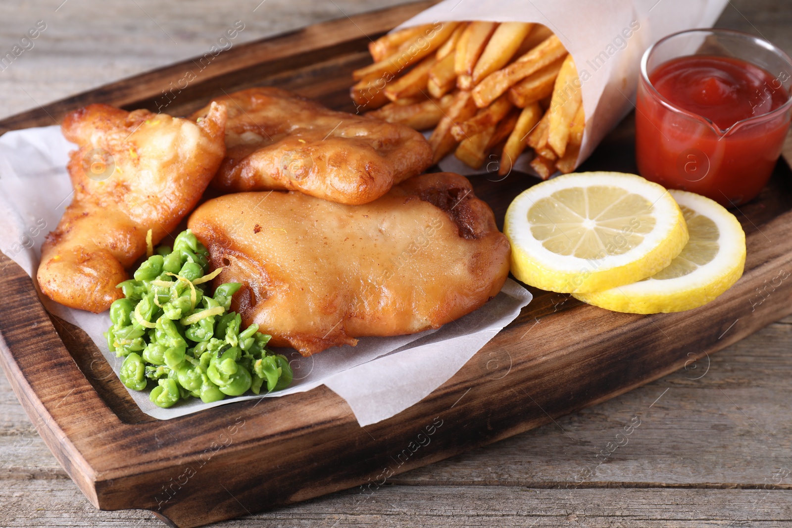 Photo of Tasty fish, chips, sauce and peas on wooden table, closeup