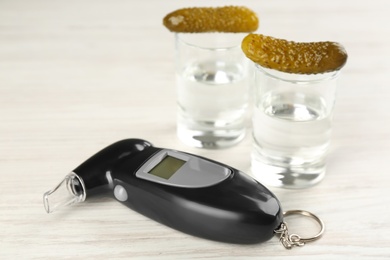 Photo of Modern breathalyzer and vodka with pickles on white wooden table