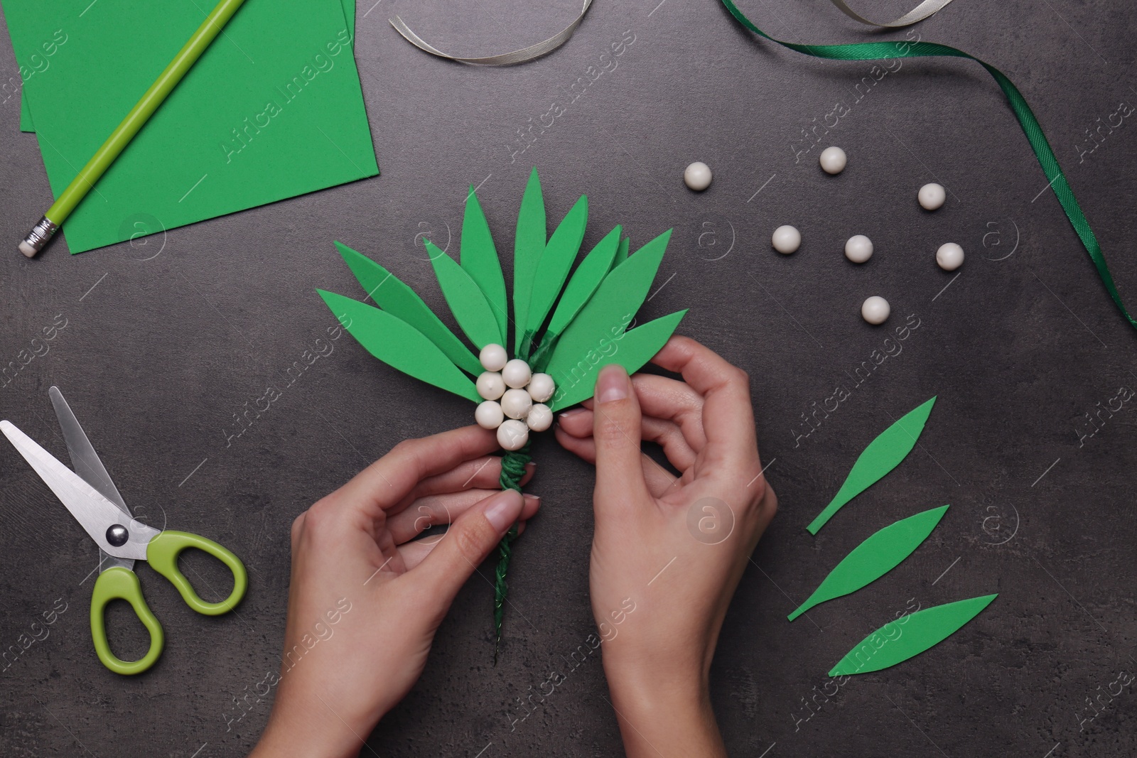 Photo of Woman making mistletoe branch on grey table, top view