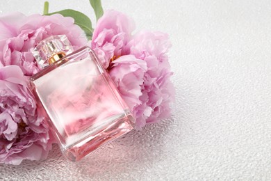 Luxury perfume and floral decor on white plastic surface, space for text