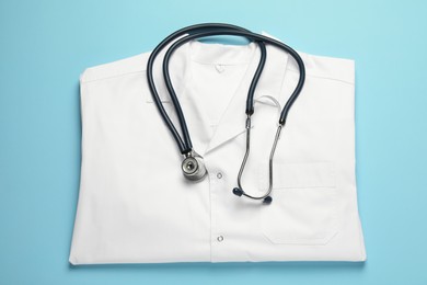 Photo of Medical uniform and stethoscope on light blue background, flat lay