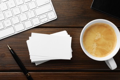 Blank business cards, coffee, keyboard and pen on wooden table, flat lay. Mockup for design