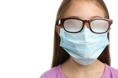 Photo of Little girl with foggy glasses caused by wearing disposable mask on white background, closeup. Protective measure during coronavirus pandemic