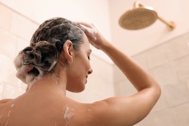 Woman washing hair while taking shower at home, back view