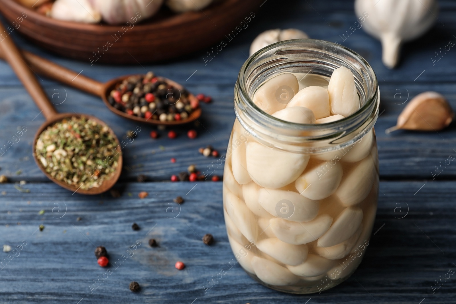 Photo of Preserved garlic in glass jar on wooden table. Space for text