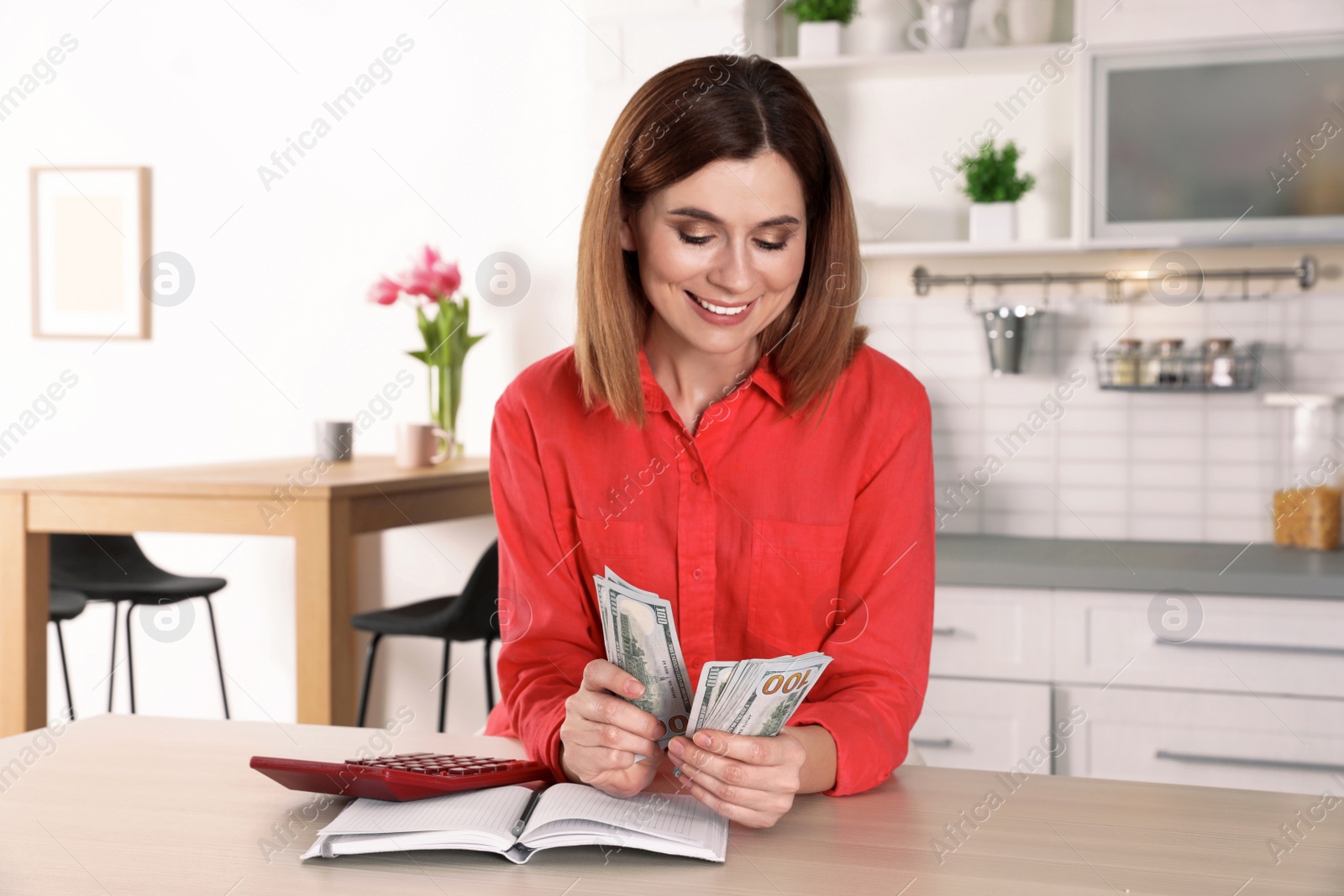 Photo of Smiling woman counting money at table indoors