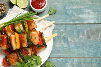 Photo of Delicious chicken shish kebabs with vegetables and ketchup on light blue wooden table, flat lay. Space for text