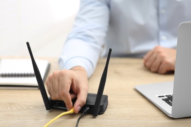 Photo of Man inserting cable into Wi-Fi router at wooden table indoors, closeup