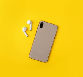 Photo of Wireless earphones and mobile phone on yellow background, flat lay. Space for text