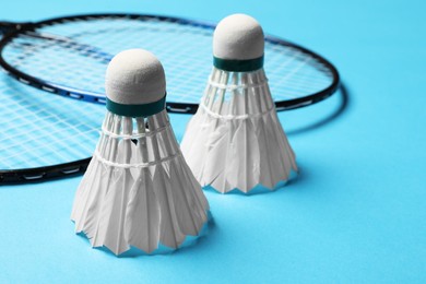 Photo of Feather badminton shuttlecocks and rackets on light blue background, closeup