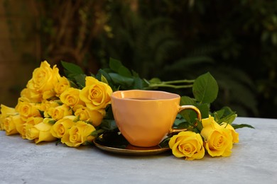 Photo of Cup of drink and beautiful yellow roses on light table outdoors, space for text