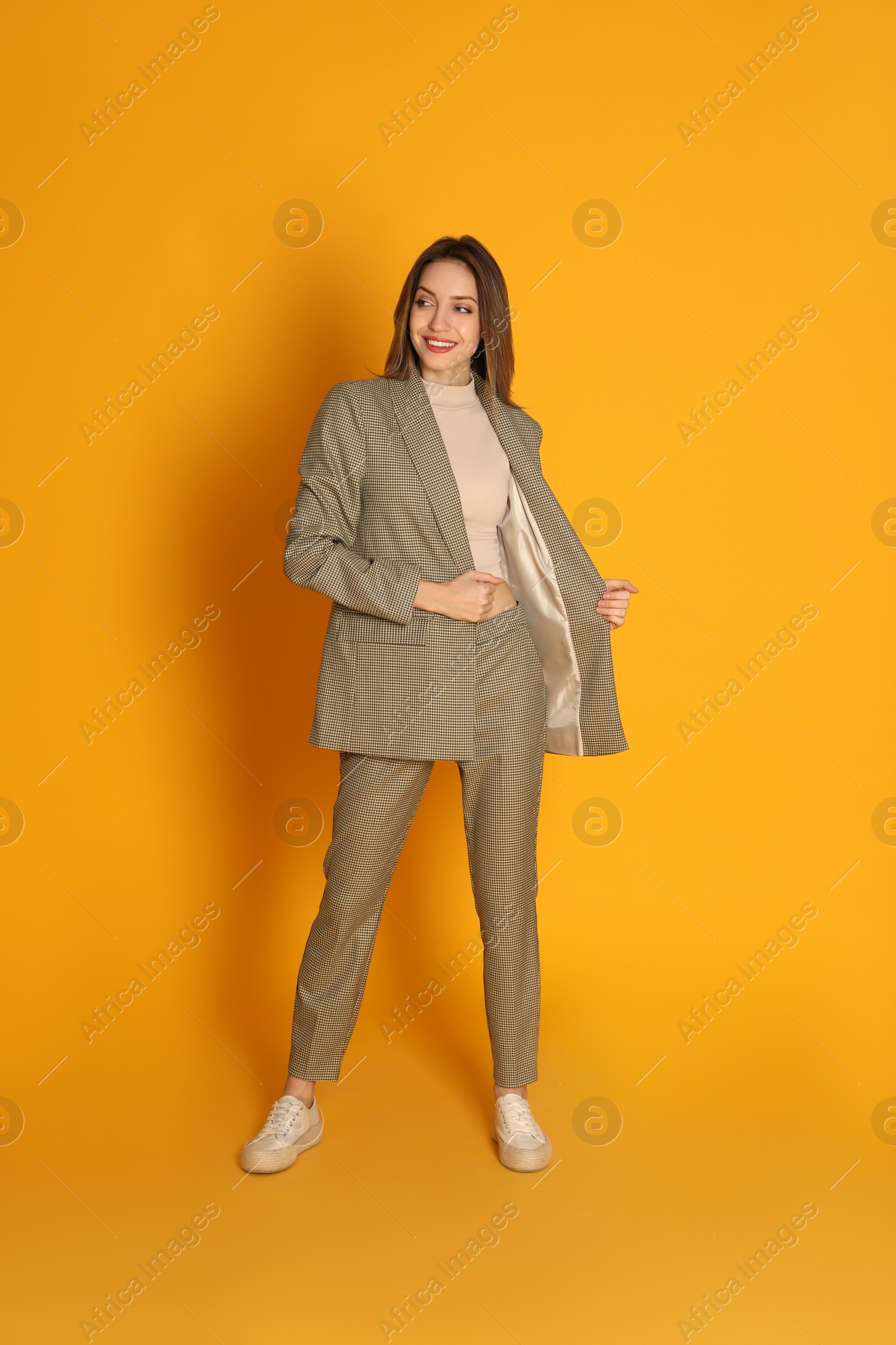 Photo of Full length portrait of beautiful young woman in fashionable suit on yellow background. Business attire