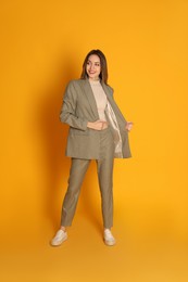 Full length portrait of beautiful young woman in fashionable suit on yellow background. Business attire
