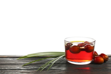 Palm oil in glass bowl with fruits and tropical leaf on black wooden table against white background