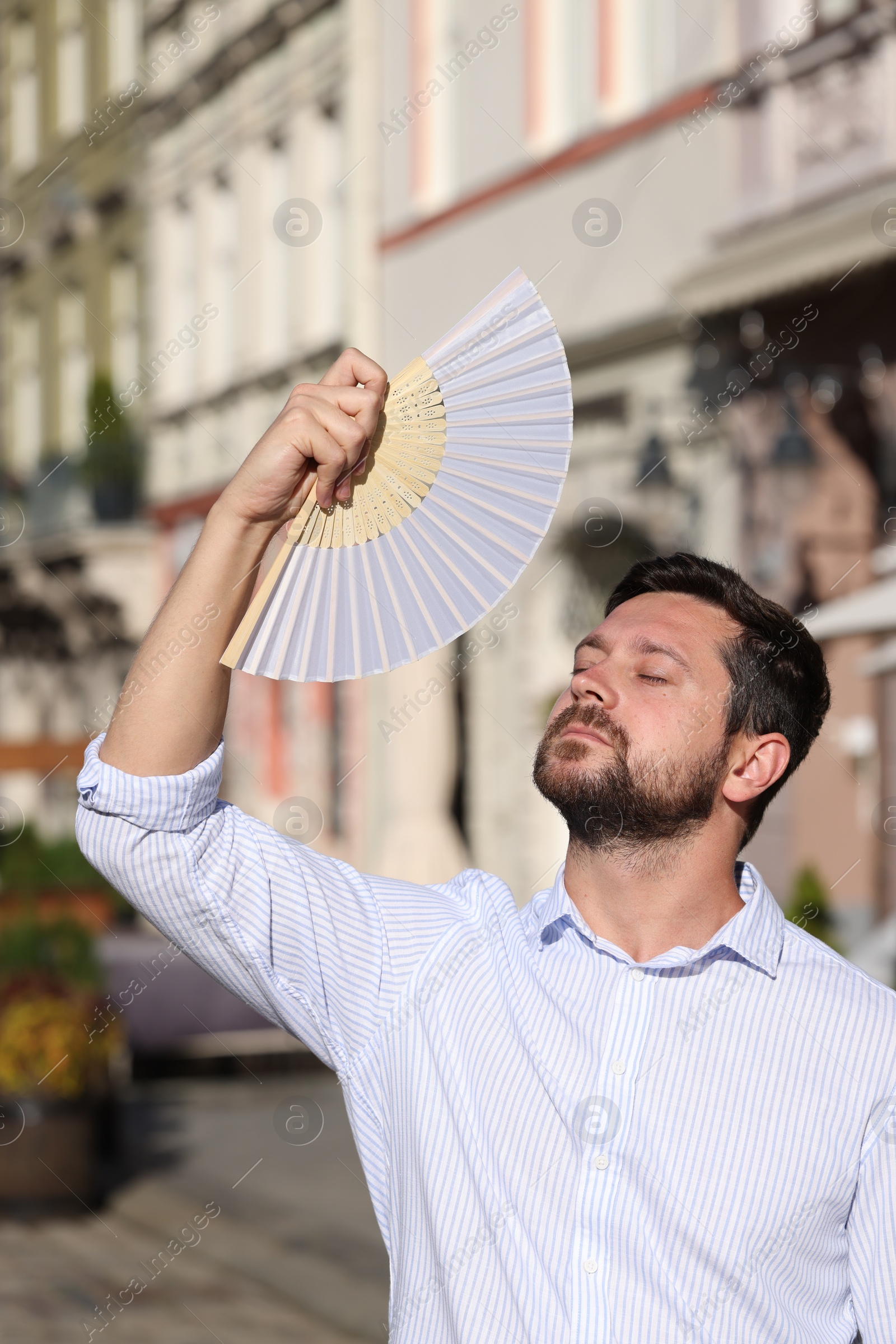 Photo of Man with hand fan suffering from heat outdoors